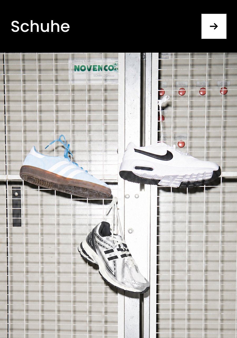 Die Beine einer Person in einer dunklen Hose und hellen Socken, die braune Leder-Loafer mit dicken schwarzen Sohlen trägt und auf Beton steht. Text: Schuhe