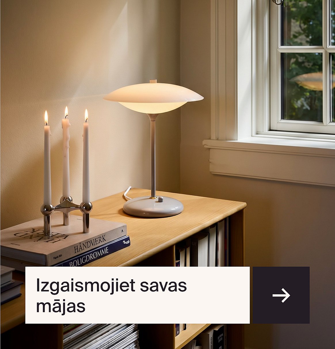 Uz koka galda ar grāmatām pie loga stāvēja ieslēgta moderna galda lampa un trīs iedegtas sveces.