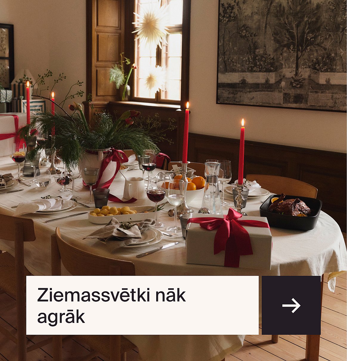 Ziemassvētku vakariņu galds, uz kura stāv degošas sarkanas sveces, mūžzaļš galda rotājums, ēdiens, vīns un dāvanu kaste.