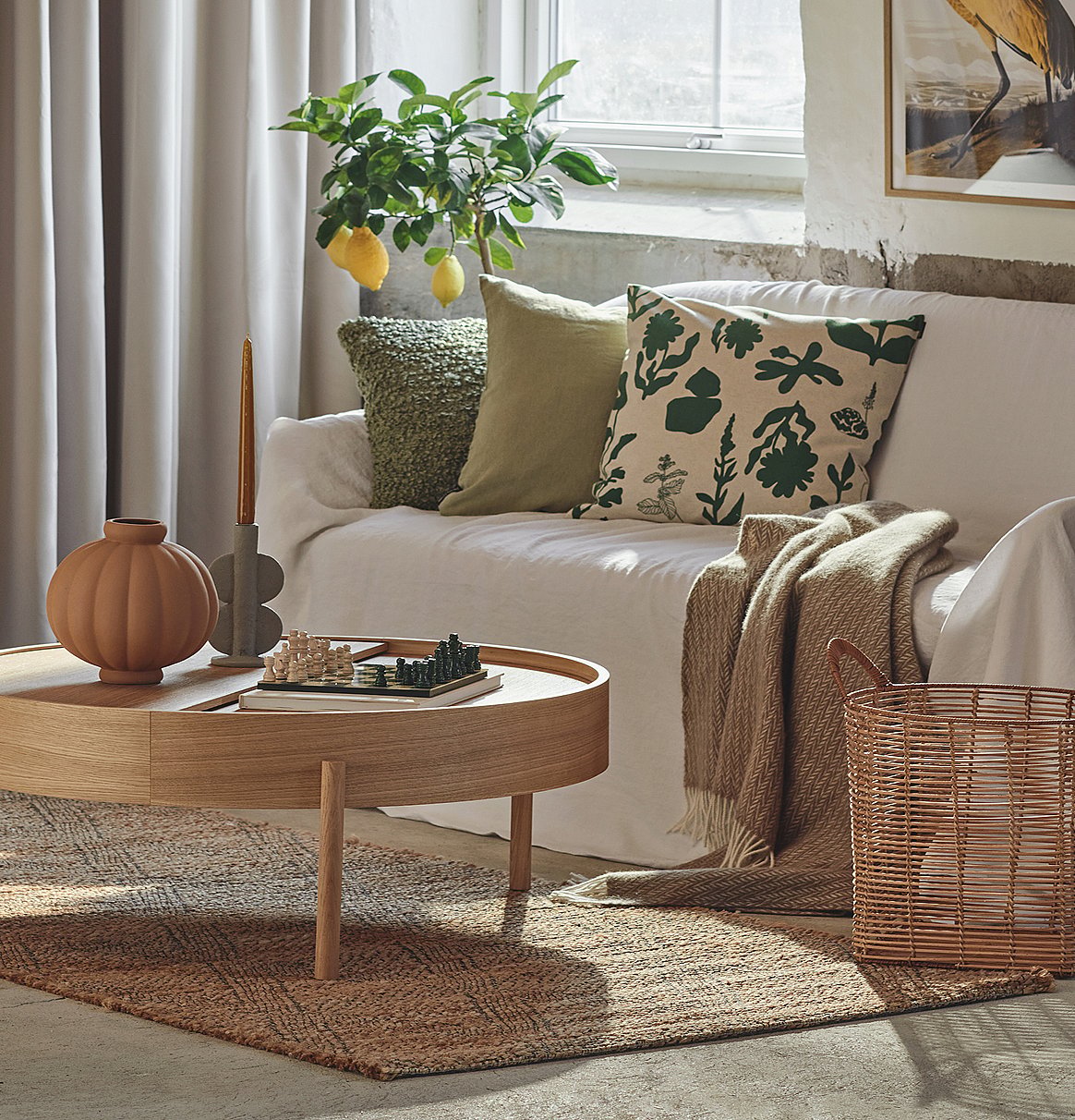 Gmüetlichs Wohnzimmer mit wiisem Sofa, grüene Chüssi, Zitronäbaum, hölzigem Couchtisch mit Schachspiil und emene Jute-Teppich.