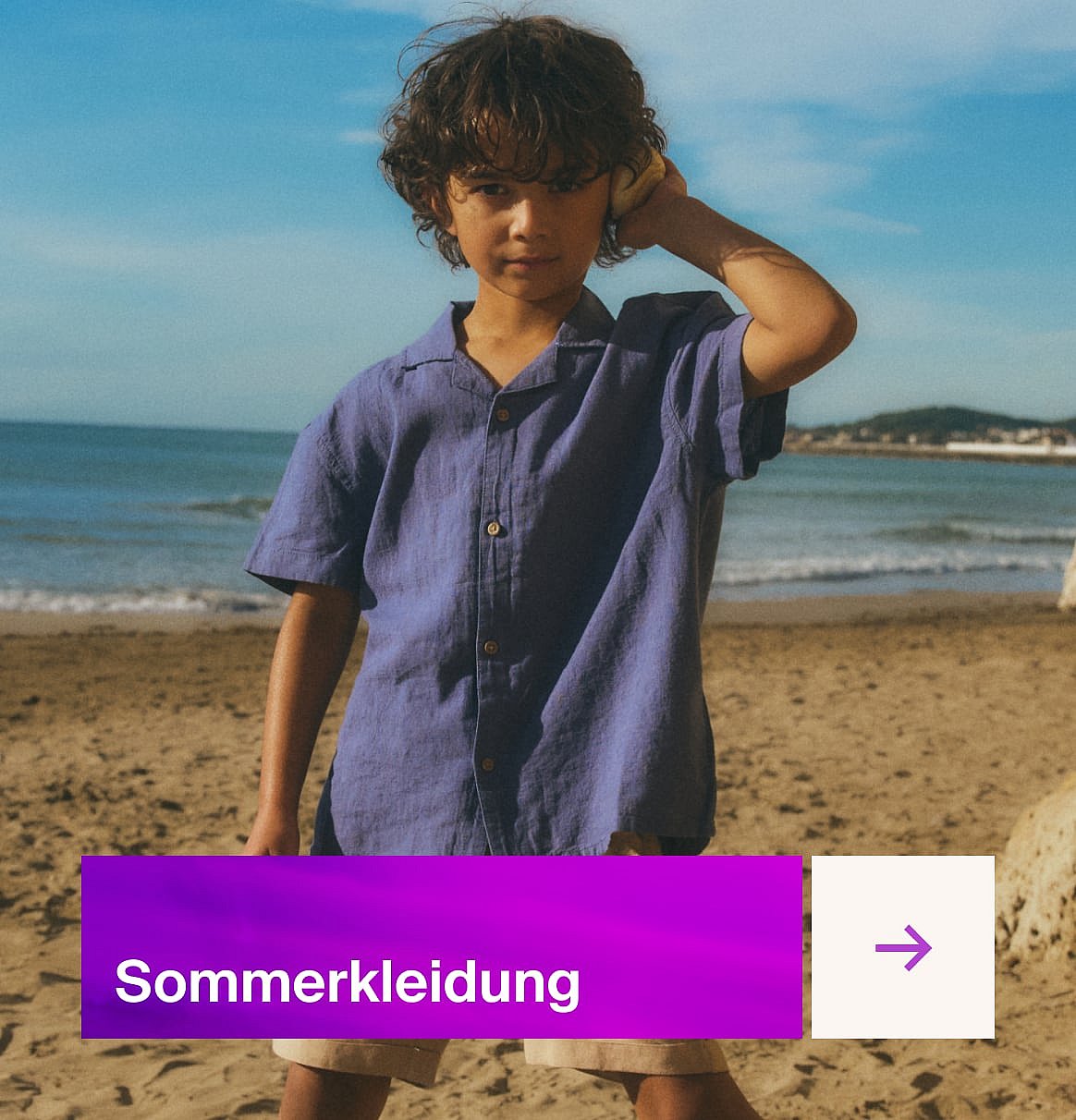 Ein Kind in einem blauen T-Shirt steht an einem sandigen Strand mit dem Meer und blauem Himmel.
Sommerkleidung.