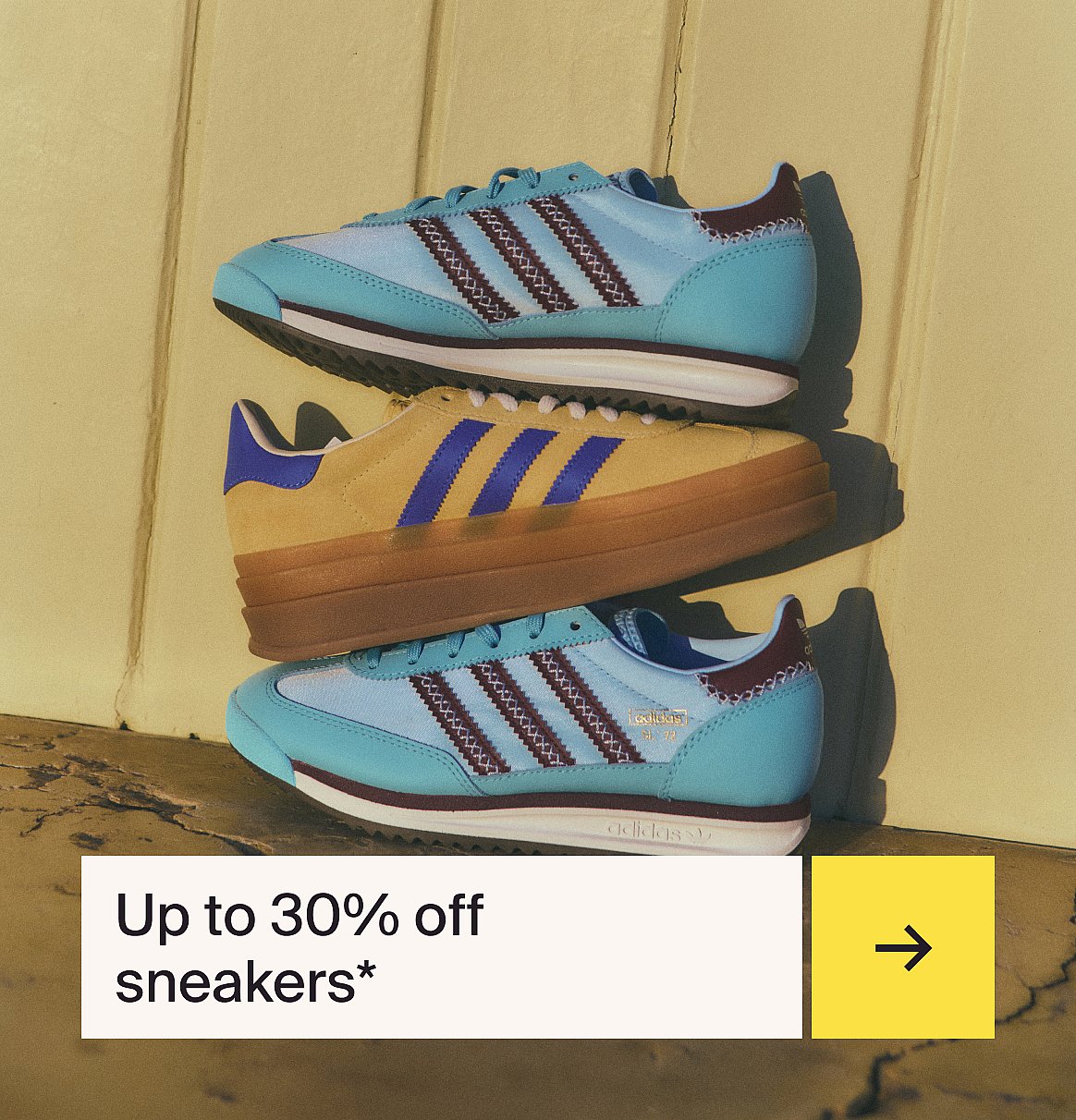 Three stacked Adidas sneakers: two light blue with maroon accents, one yellow with blue accents, on a yellow surface.