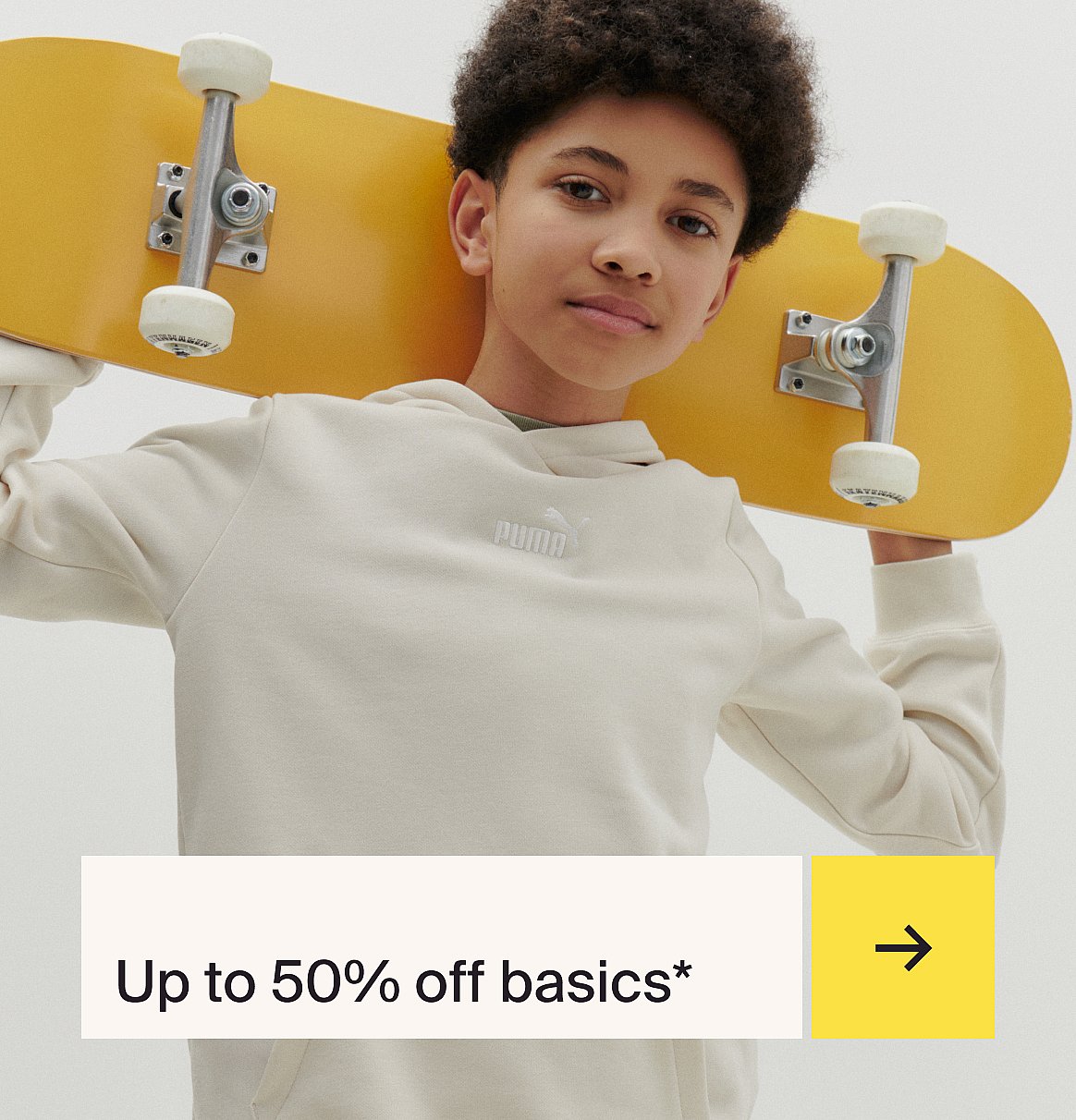 Young person in a light Puma hoodie holds a yellow skateboard over their shoulder, looking at the camera.