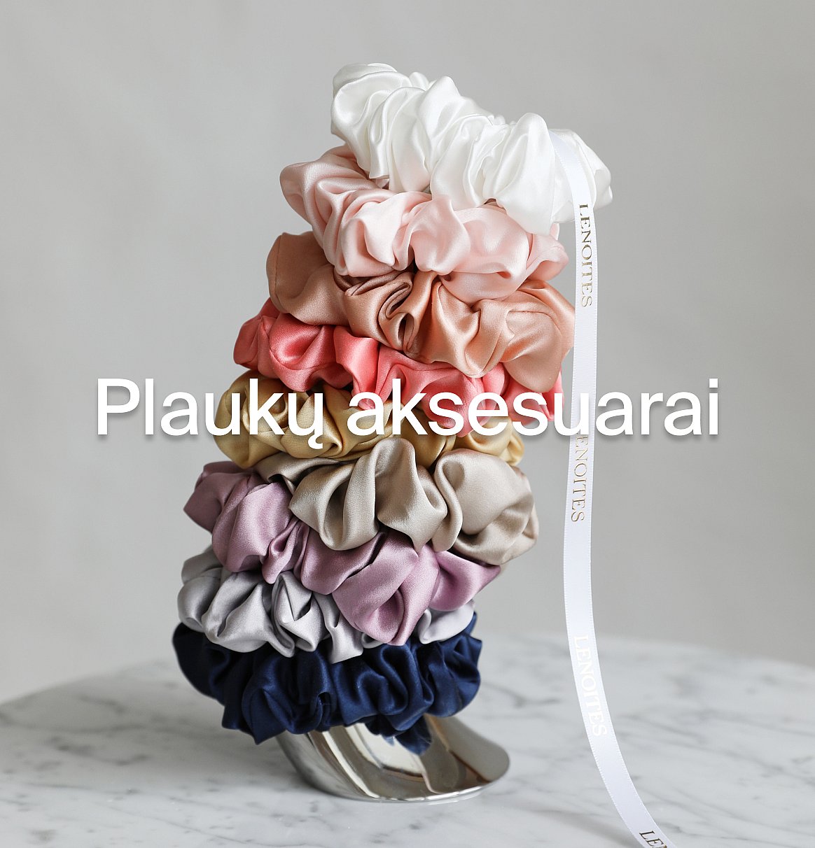 Daugiaspalvės plaukų gumelės, sudėtos ant marmuro paviršiaus, su baltu kaspinu.
Plaukų aksesuarai.