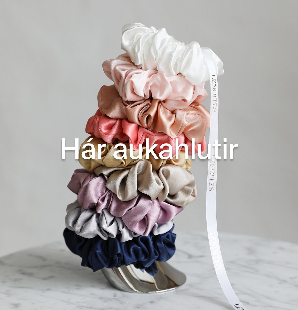 Marglitar hárteygjur staflaðar á marmaraflöt, með hvítum borða.
Hárskraut.