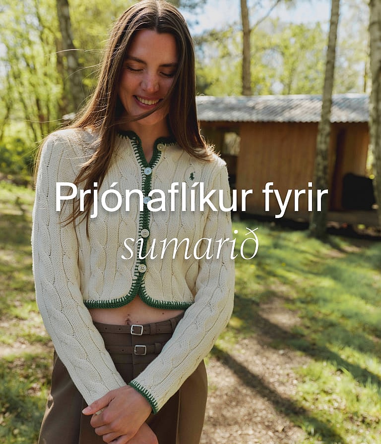 Brosandi kona í rjómabláum kaðalprjónuðum jakkapeysu með grænum kanti, í skógi með sumarbústað.
Sumarprjónafatnaður