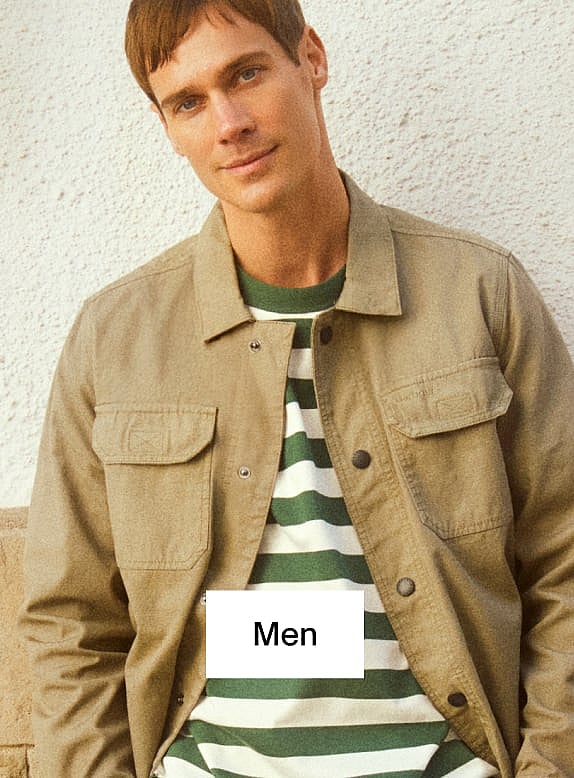 Man in tan jacket and green and white striped shirt, leaning against a light wall. Text overlay: Men.
