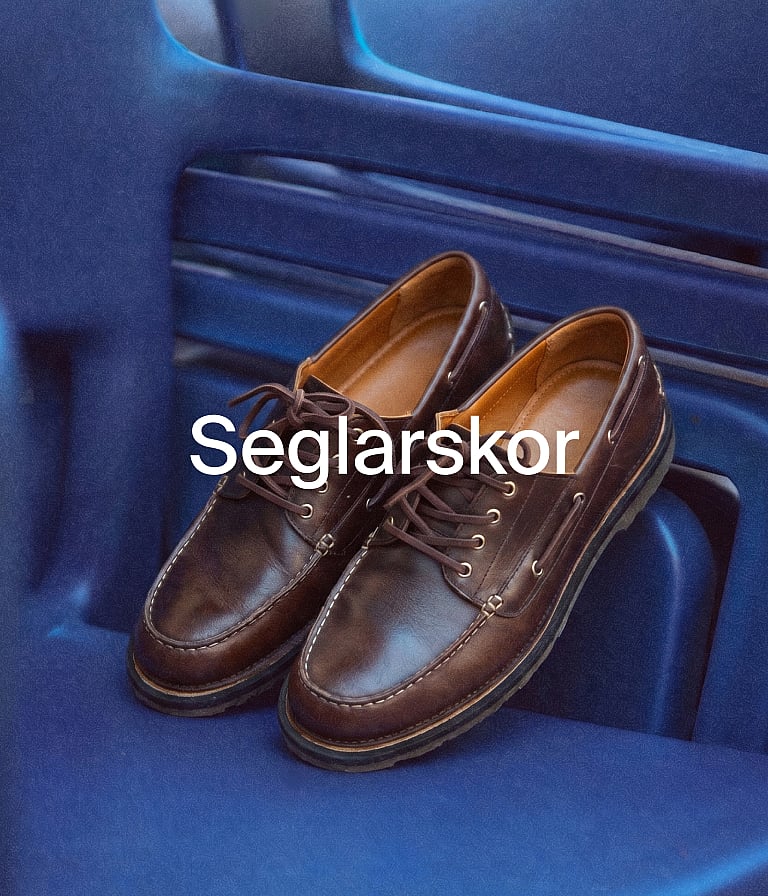 Ett par bruna läderbåtskor vilar på en blå yta. Vit textöverlagring lyder "Båtskor".