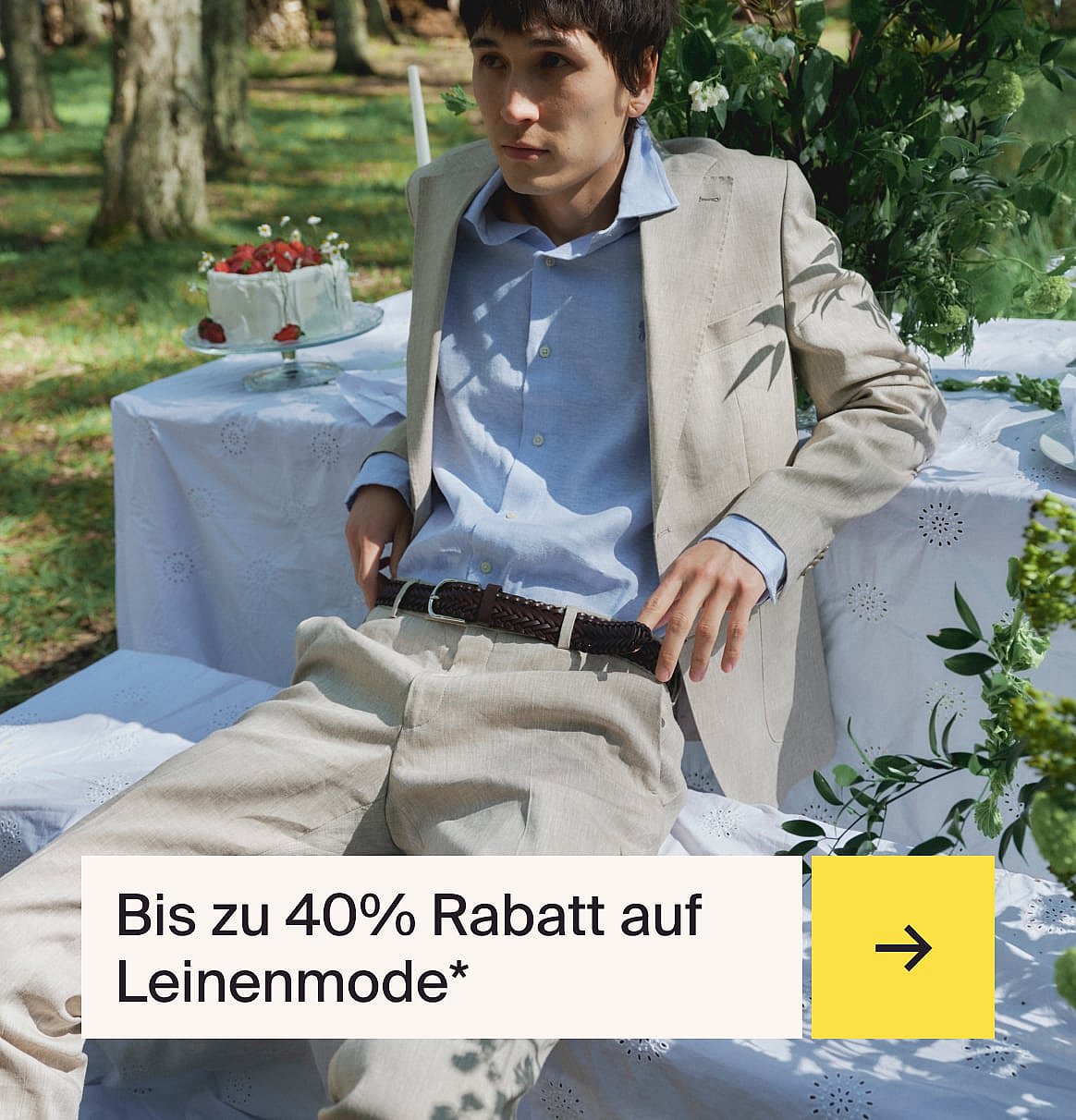 Mann in hellblauem Hemd und beigem Leinenanzug sitzt an einem Außentisch im Garten mit einem Erdbeerkuchen.
