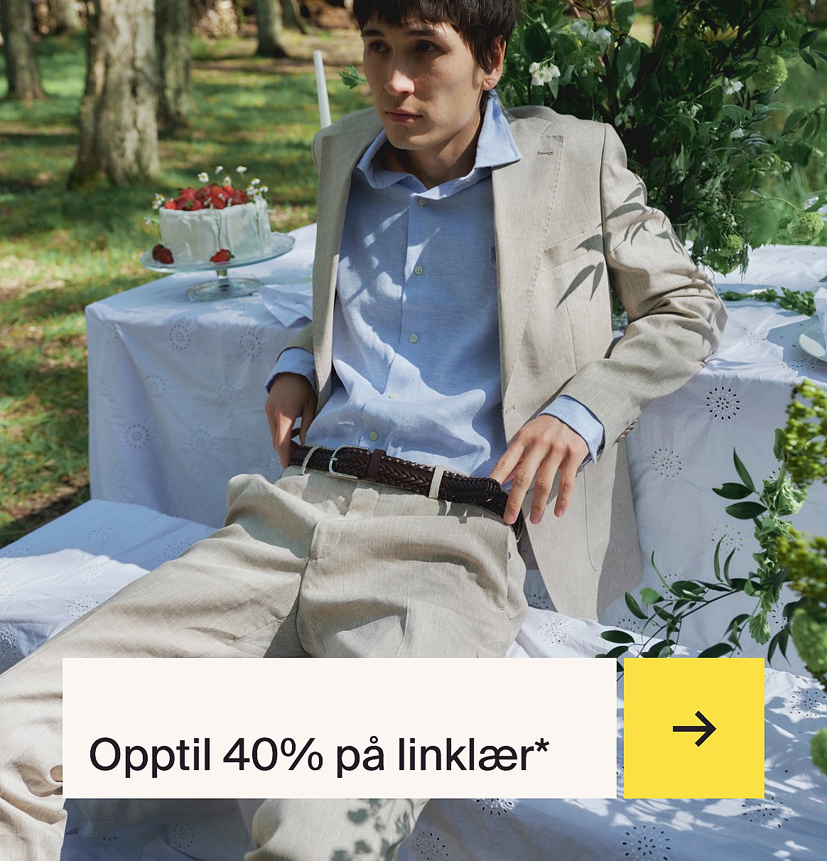 Mann i lyseblå skjorte og beige lindress sitter ved et utebord med en jordbærkake i en hage.