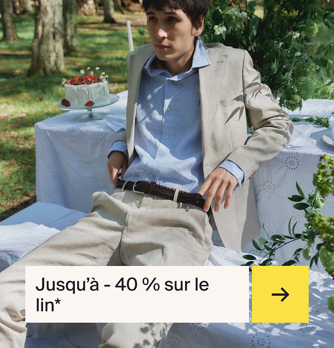 Homme en chemise bleu clair et costume en lin beige assis à une table en extérieur avec un gâteau aux fraises dans un jardin.