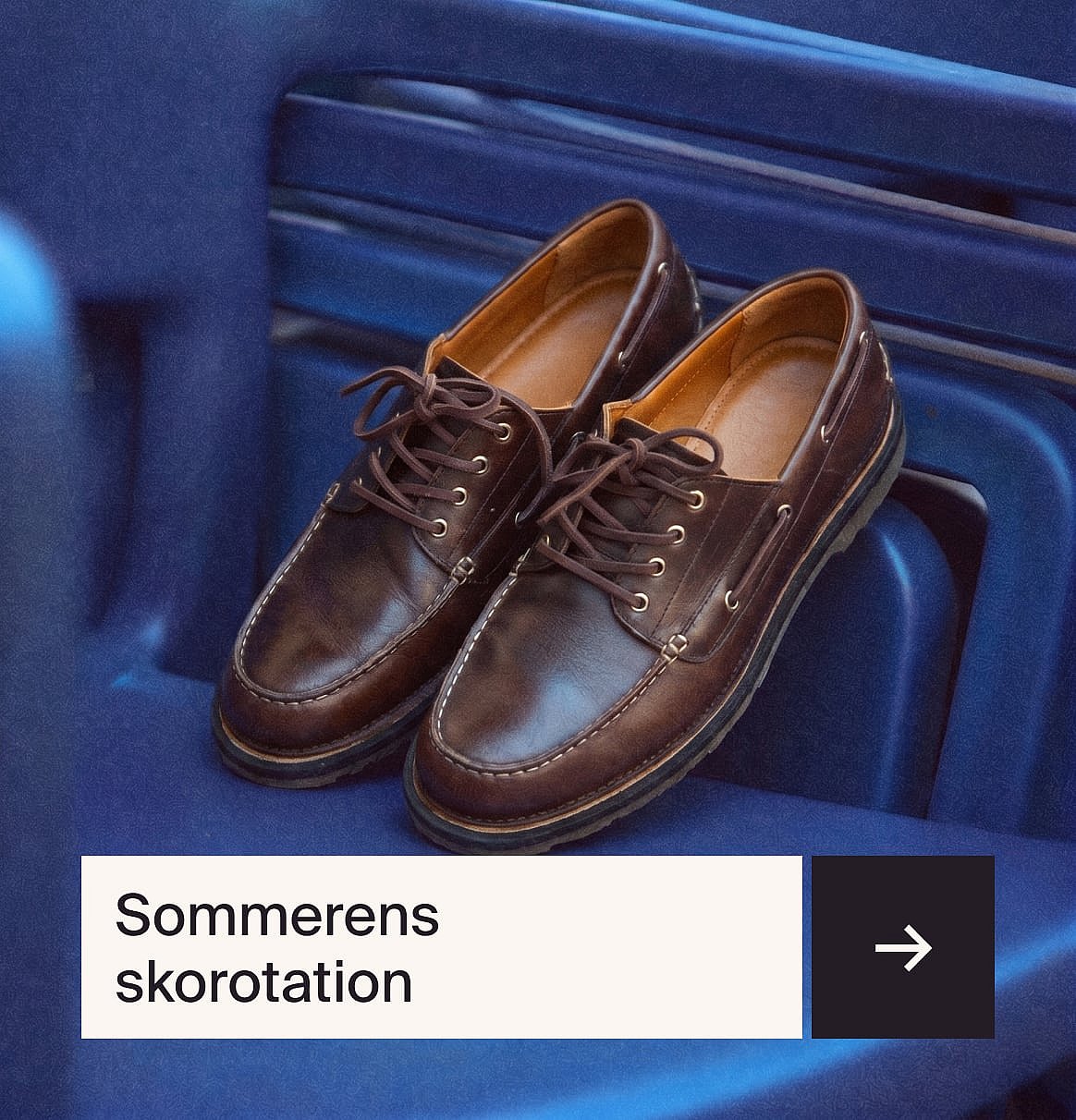 Et par brune snøresko i læder i mokkasin-stil med hvide syninger, der hviler på en blå ribbet overflade.