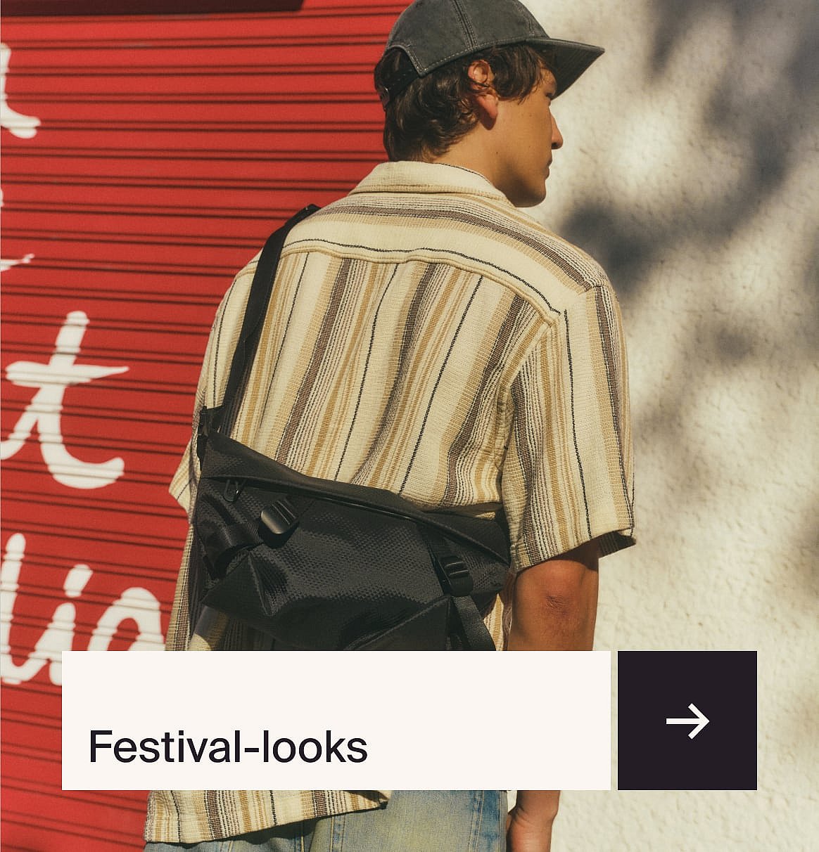 Mann i stripete skjorte, caps og svart crossbody-veske, sett bakfra, mot røde og hvite vegger. «Festival-looks»