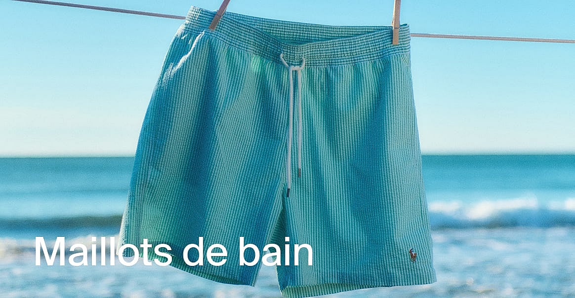Des shorts de bain rayés bleu sarcelle sont suspendus à une corde à linge, avec une plage ensoleillée et l'océan en arrière-plan. Découvrez les shorts de bain.