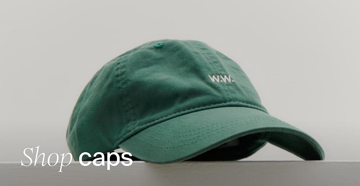 Green baseball cap with white 'W.W.' logo, resting on a surface against a light background. Text: 'Shop caps'.