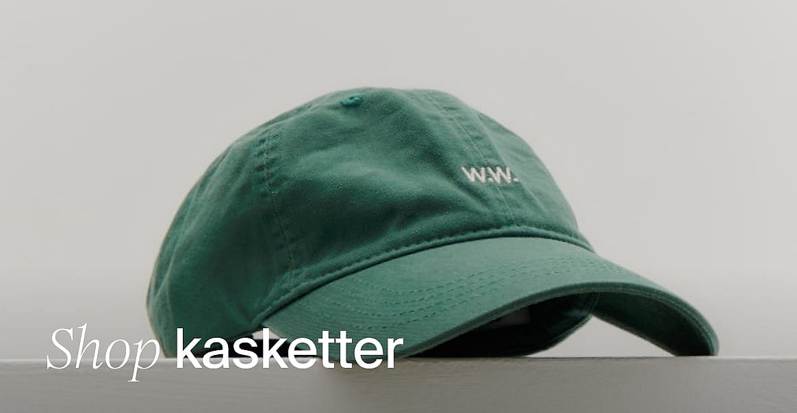 Grøn baseballkasket med hvidt 'W.W.'-logo, liggende på en overflade mod en lys baggrund. Tekst: 'Shop kasketter'.