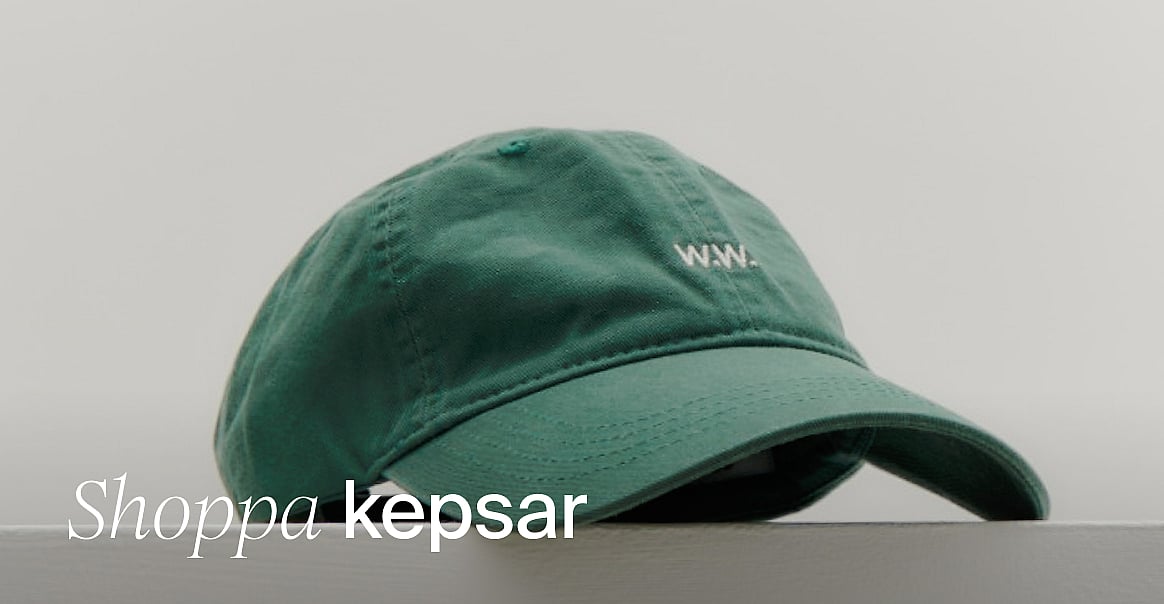 Grön baseballkeps med vit 'W.W.'-logga, ligger på en yta mot en ljus bakgrund. Handla kepsar.