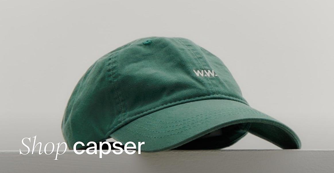 Grønn baseballcaps med hvitt «W.W.»-logo, ligger på et underlag mot en lys bakgrunn. Handle caps.