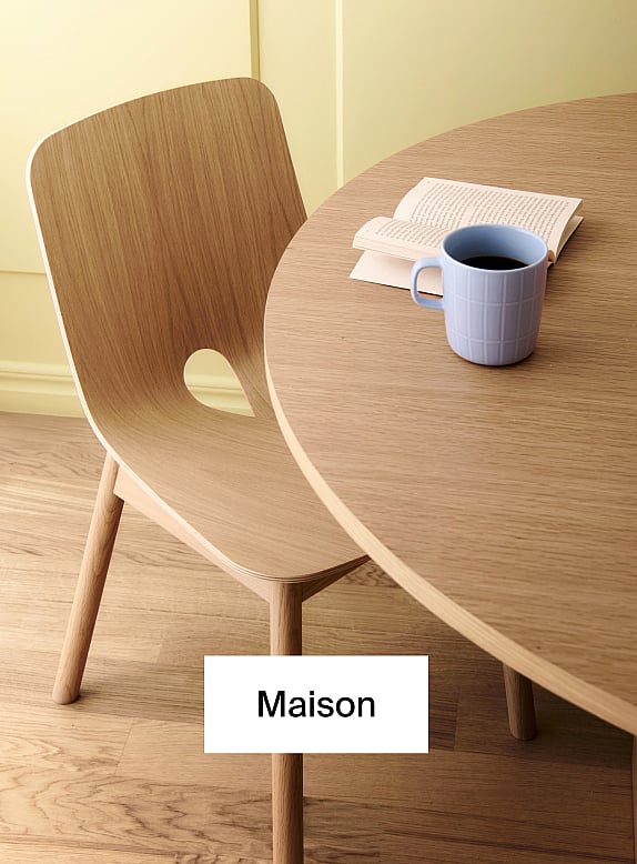 Chaise en bois clair et table ronde. Tasse à café bleue, livre ouvert sur la table. Mur jaune, plancher en bois.