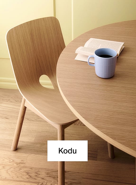 Hele puidust tool ja ümar laud. Sinine kohvikruus, avatud raamat laual. Kollane sein, puidust põrand.