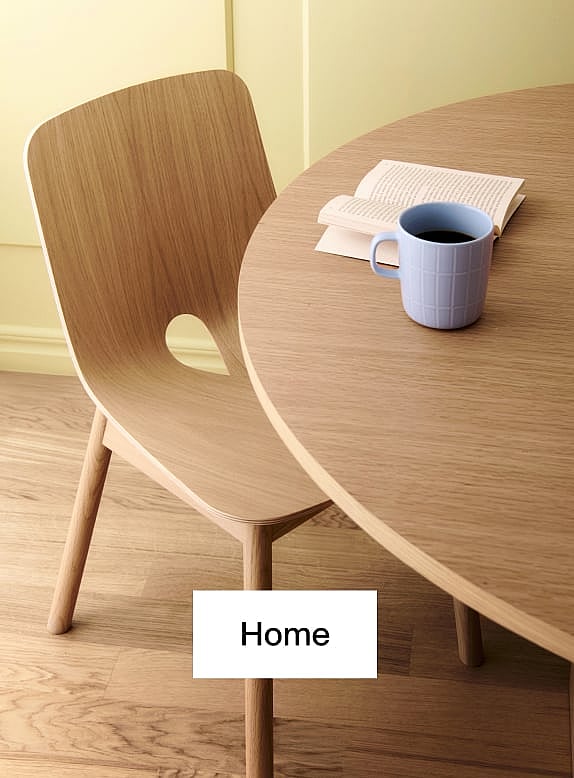Lichte houten stoel en ronde tafel. Blauwe koffiemok, open boek op tafel. Gele muur, houten vloer.