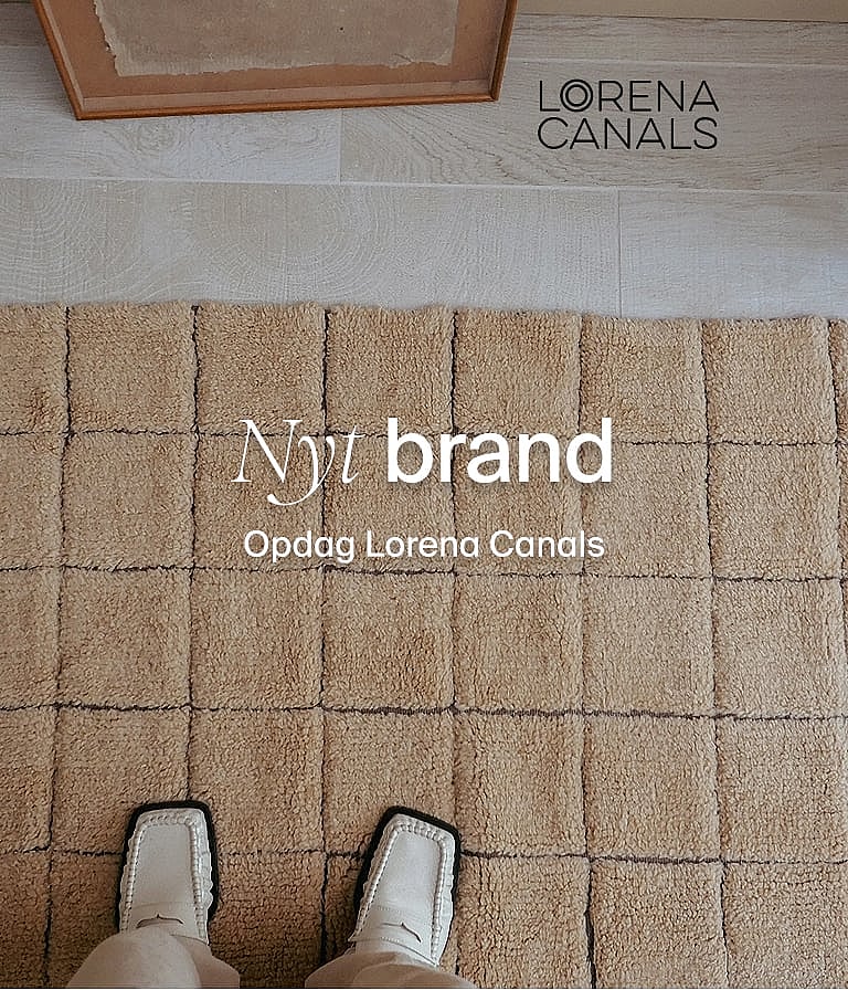 Fødder i hvide sko på et tekstureret beige tæppe med hævede firkantede felter. Nyt brand: Opdag Lorena Canals.