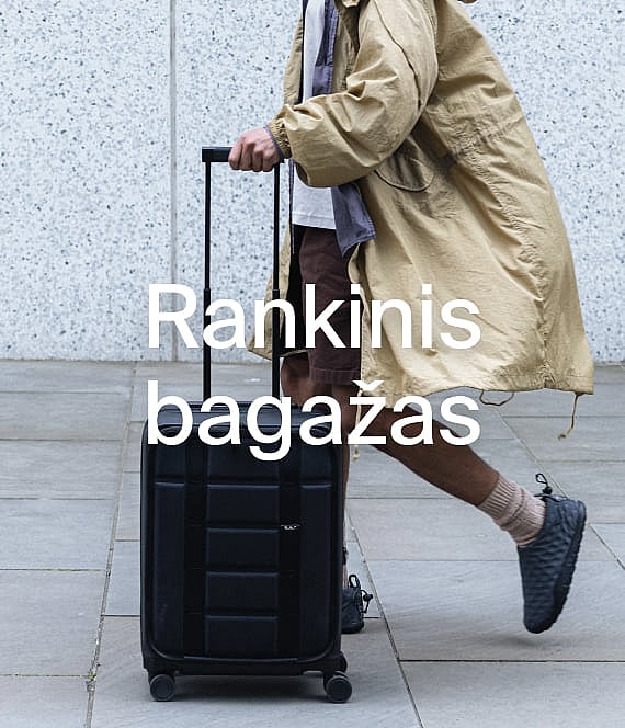 Žmogus su smėlio spalvos paltu traukia juodą rankinį lagaminą grįstu taku.
**Rankiniai lagaminai.**