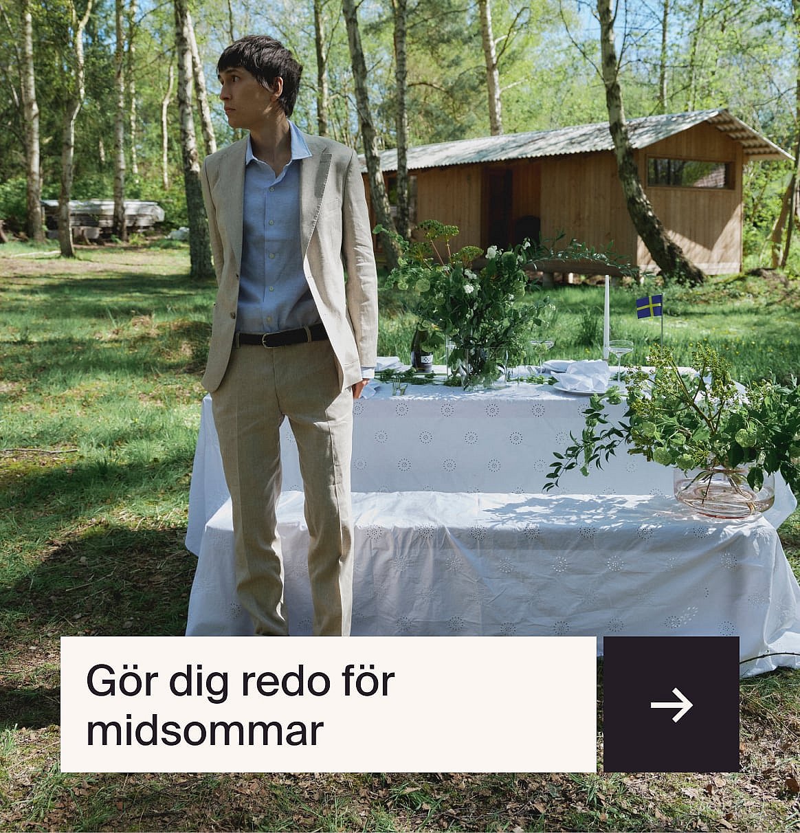 Man i ljusblå skjorta och beige linnekostym sitter vid ett utomhusbord med en jordgubbstårta i en trädgård.