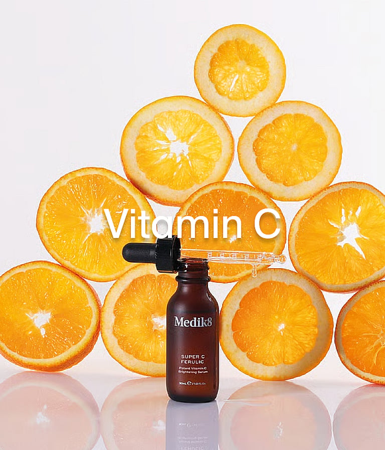 Medik8 Super C Ferulic serum bottle with dropper, surrounded by a pyramid of orange slices. White "Vitamin C" text.