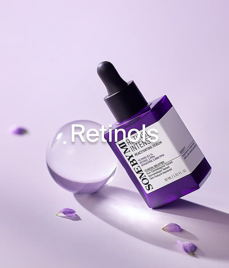Violeta SOME BY MI Retinola seruma pudele ar pipeti, caurspīdīga sfēra un izkaisītas ziedlapiņas uz gaiši violetas virsmas.