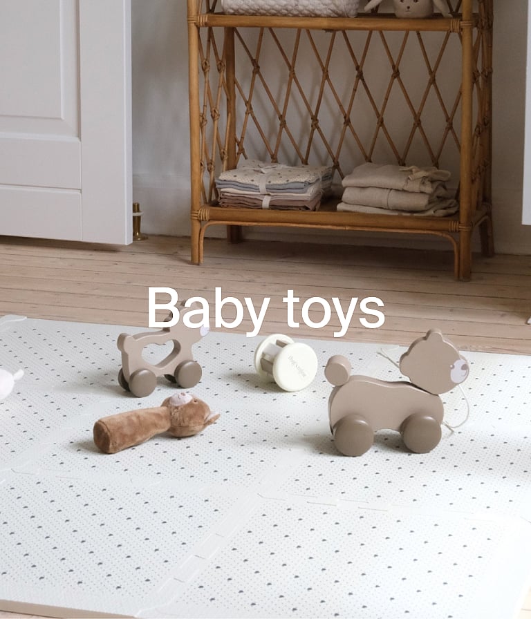 Two wooden pull-along toys, rattle, and plush toy on a dotted playmat. Rattan shelf and wooden floor behind.