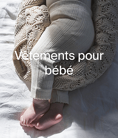 Baby's legs and feet in light patterned leggings, on a white sheet with a knitted blanket. Text: Vêtements pour bébé.