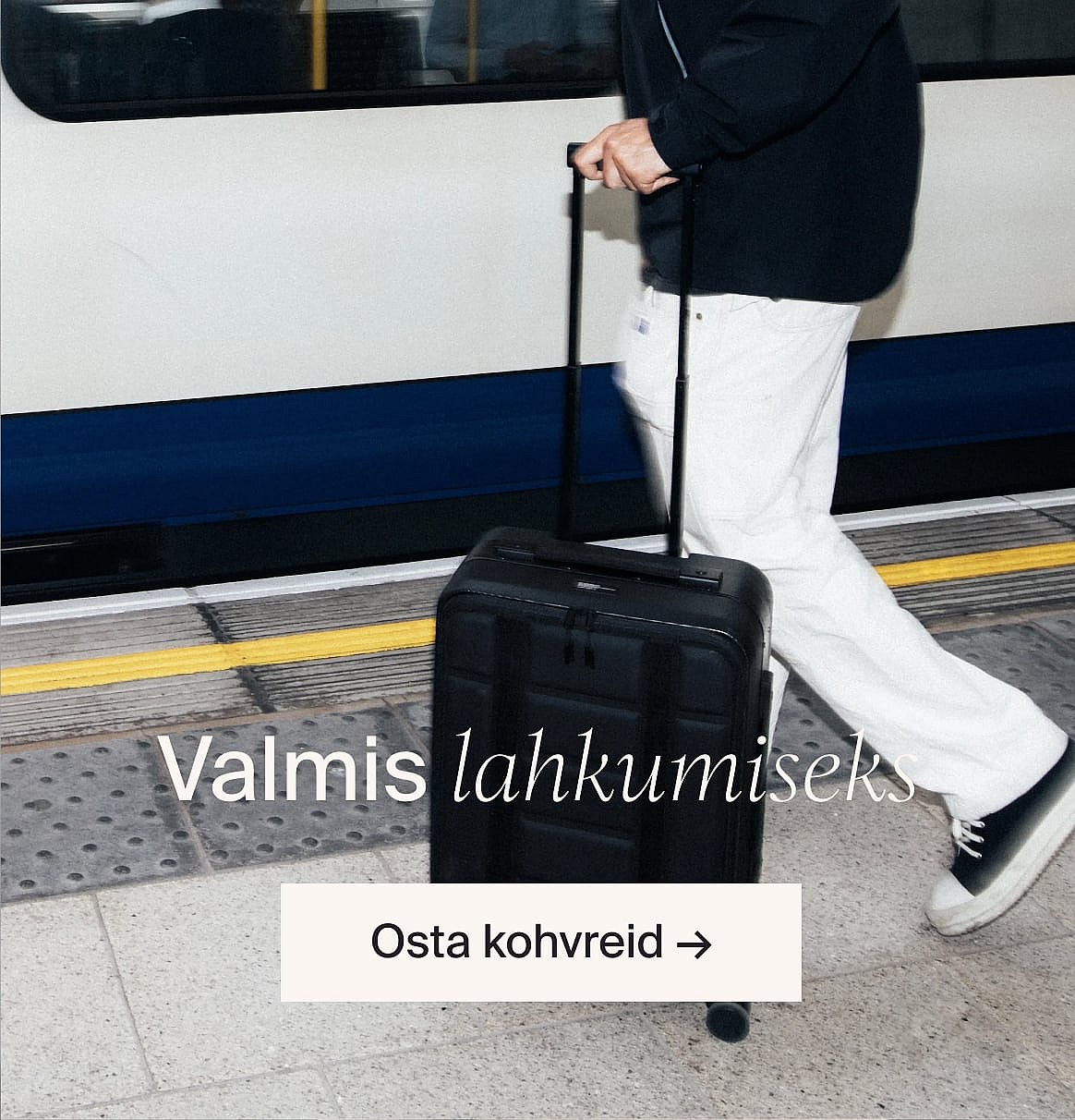 Valges lühikeste varrukatega broderiisärgis ja sinistel teksapükstes, käed taskutes, seistes heleda puitseina vastu.