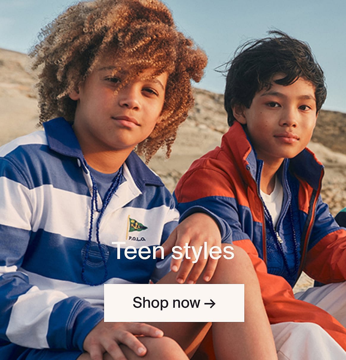 Two boys, one with curly hair in a striped polo, one in a red and blue jacket, sitting outdoors. Text: Teen styles, Shop now.