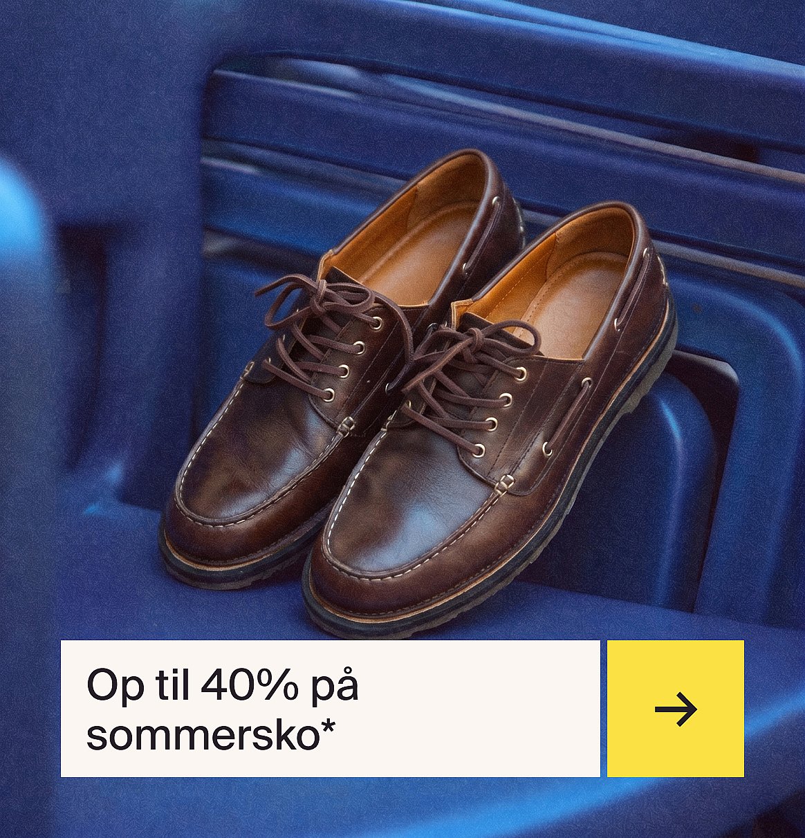 Et par brune snøresko i læder i mokkasin-stil med hvide syninger, der hviler på en blå ribbet overflade.