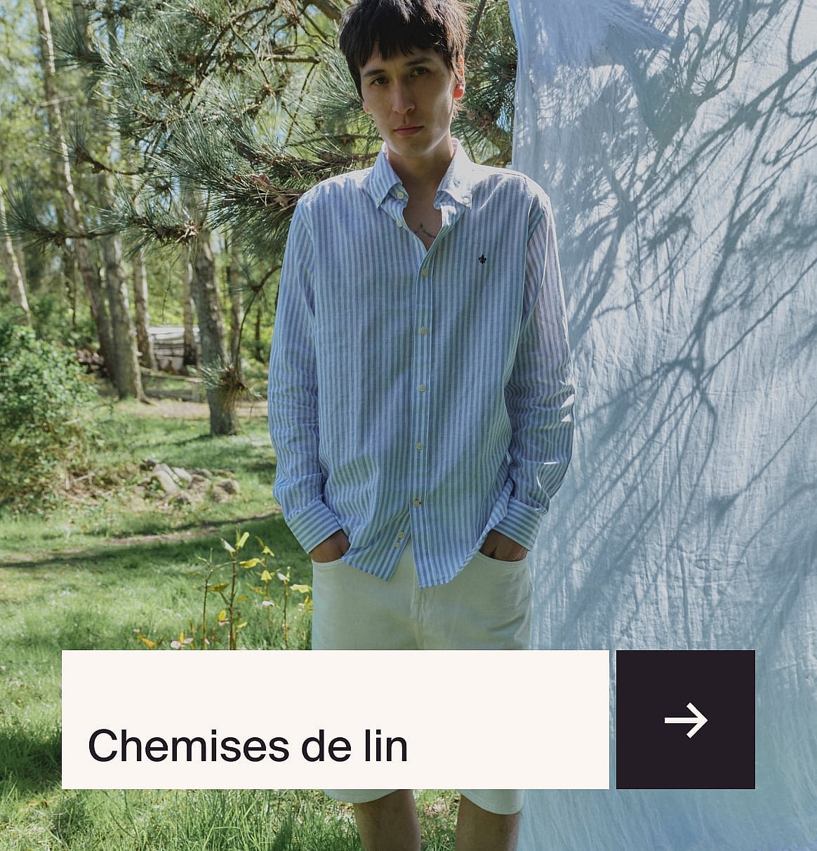 Homme en chemise bleu clair et costume en lin beige assis à une table en extérieur avec un gâteau aux fraises dans un jardin.