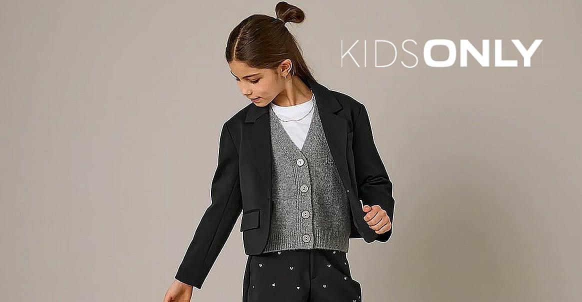 Young girl in black blazer, grey cardigan, white t-shirt, and dark heart-patterned pants. Plain background, "KIDS ONLY" logo.
