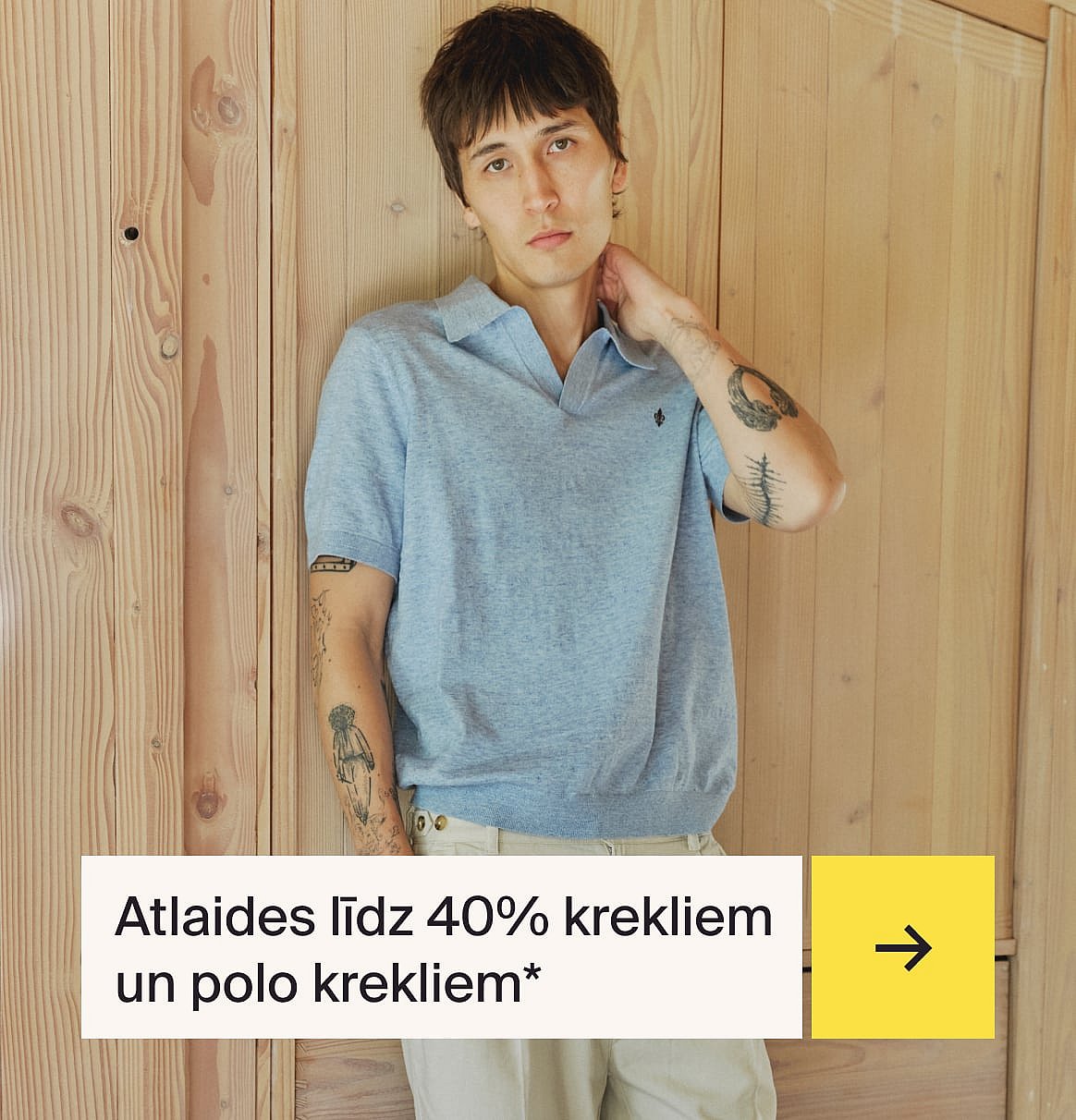 Vīrietis gaiši zilā kreklā un bēšā lina uzvalkā sēž pie āra galda ar zemeņu kūku dārzā.