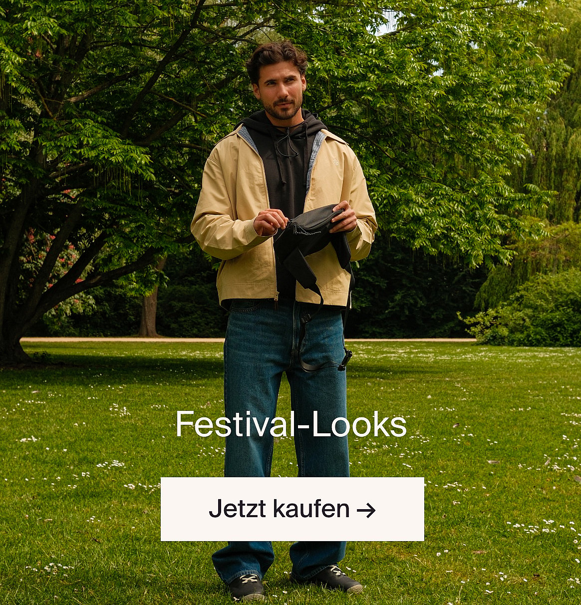 Modell in weisser Kurzarm-Bluse mit Lochstickerei und blauer Jeans, Hände in den Taschen, vor einer hellen Holzwand.
