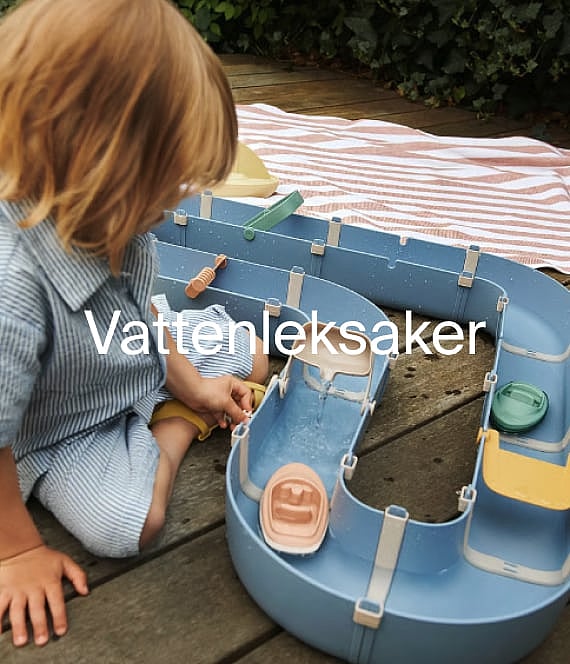 Young child playing with a blue water track toy and boats on an outdoor wooden deck.