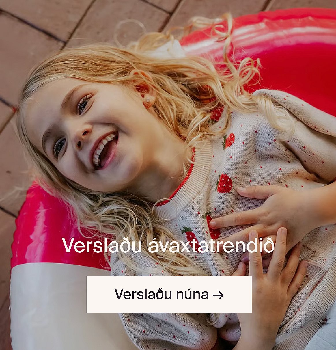 Smiling blonde girl lying on a red and white inflatable, wearing a strawberry sweater.
