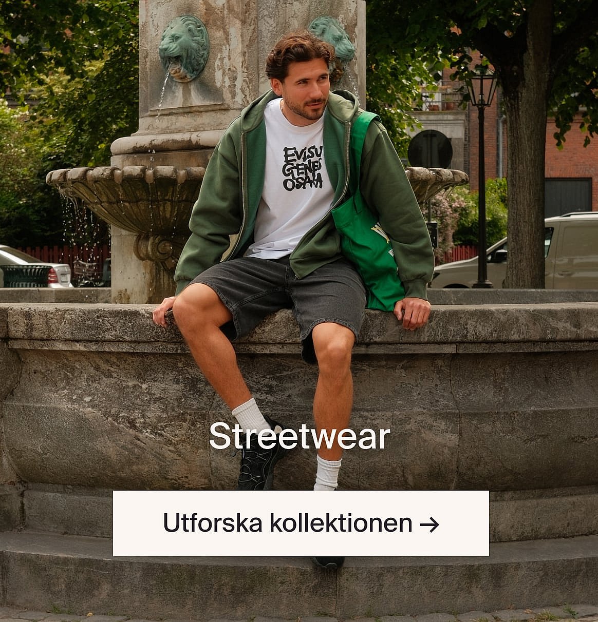 Person i vit kortärmad broderie anglaise-skjorta och blå jeans, händerna i fickorna, står mot en ljus trävägg.