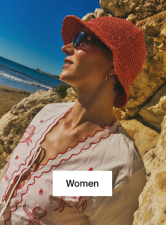 Smiling woman with curly hair, striped shirt, holding a beige bag, against a textured wall. Text overlay: Women.