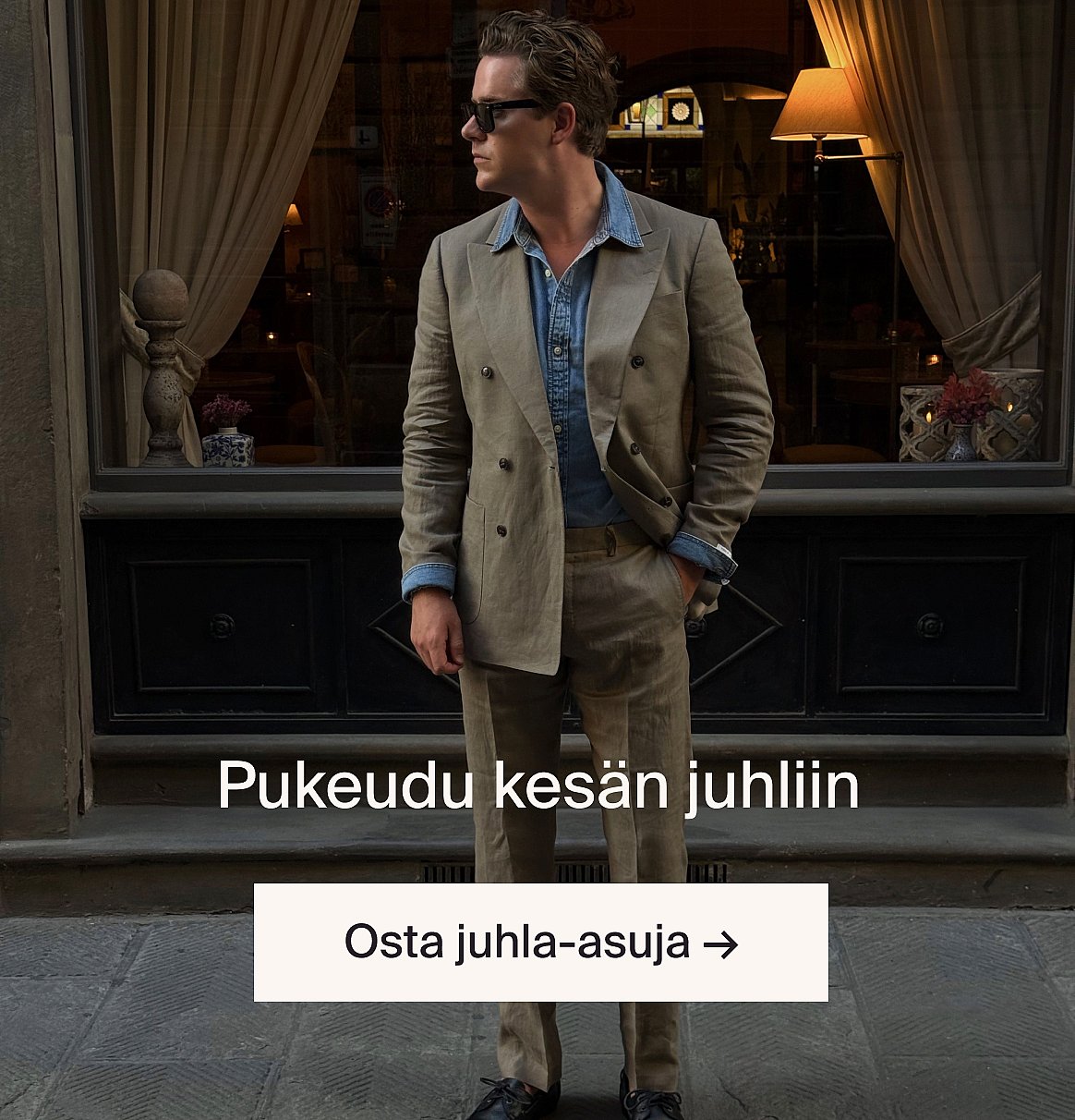 Valkoiseen reikäbrodeerattuun lyhythihaiseen paitaan ja sinisiin farkkuihin pukeutunut henkilö, kädet taskuissa, seisoo vaaleaa puuseinää vasten.