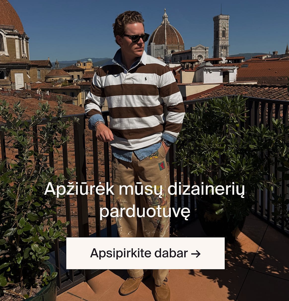 Vyras su šviesiai smėliniu kostiumu ir mėlynais marškiniais lauke, prie stalo su žaluma, miško proskynoje.