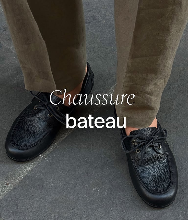 Personne en short marron, haut blanc et veste bleue, tenant des végétaux, en extérieur, devant un mur en bois.