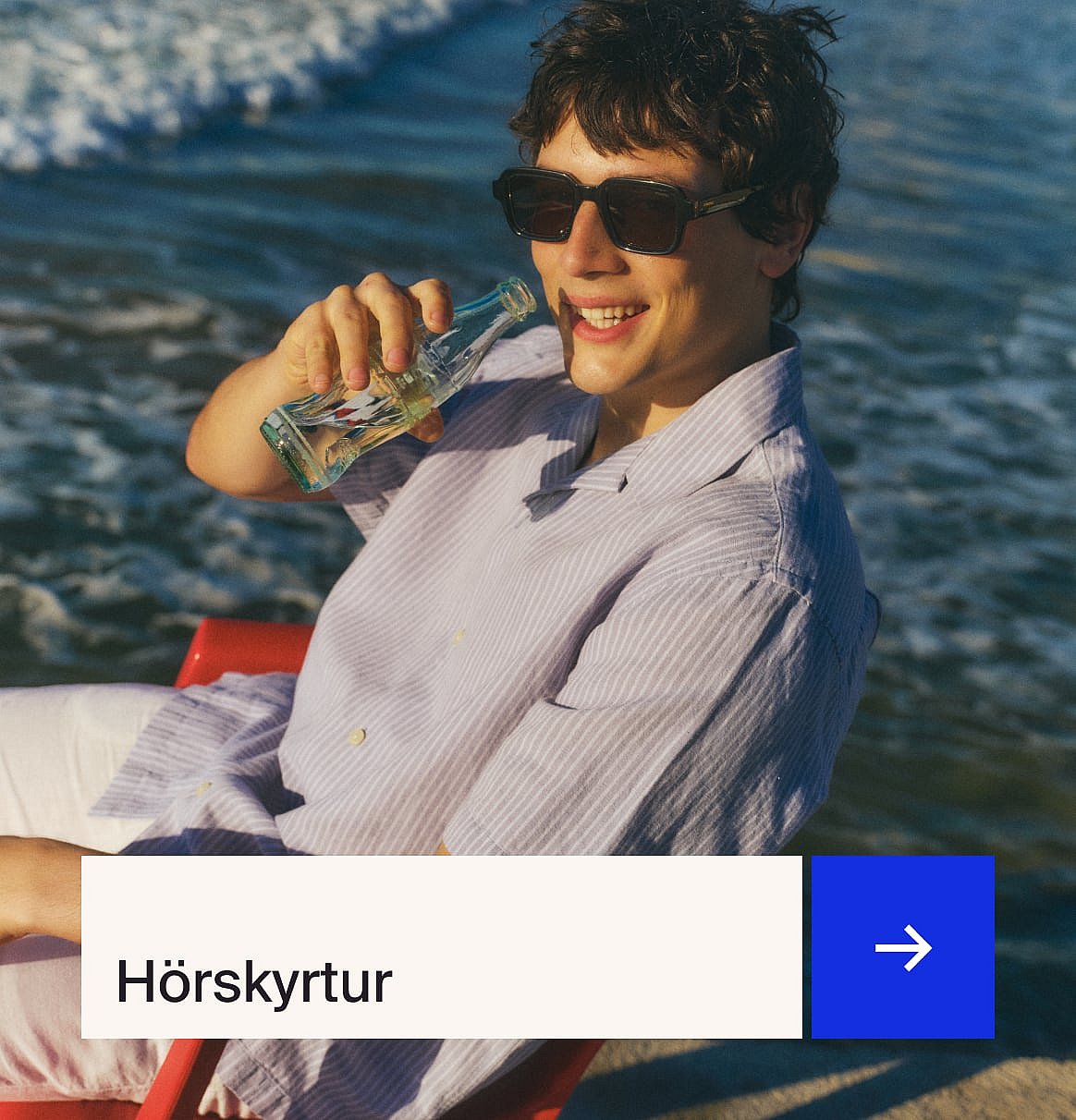 Maður í ljósblárri skyrtu og drapplitaðri línjakkafötum sitjandi við útiborð með jarðarberjaköku í garði.
