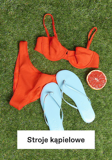 Pomarańczowe bikini, jasnoniebieskie klapki i połówka grejpfruta ułożone na zielonej trawie.
