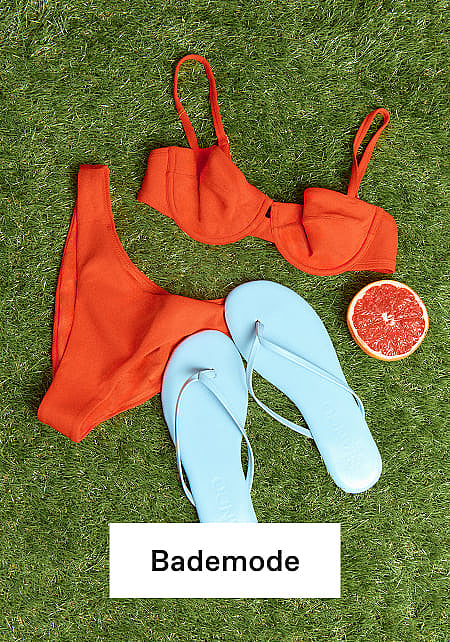 Gestreifter Shopper mit orangen Flip-Flops, Sonnenbrille, Buch und Handtuch auf grünem Gras. Sommer-Essentials.