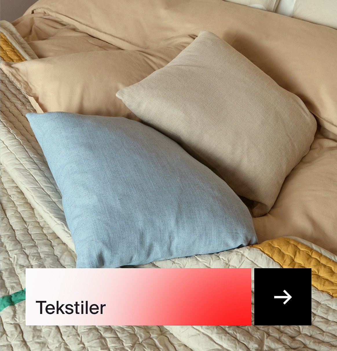 Lyseblå og beige puter av lin på en seng med beige laken og et kremfarget vattert teppe.